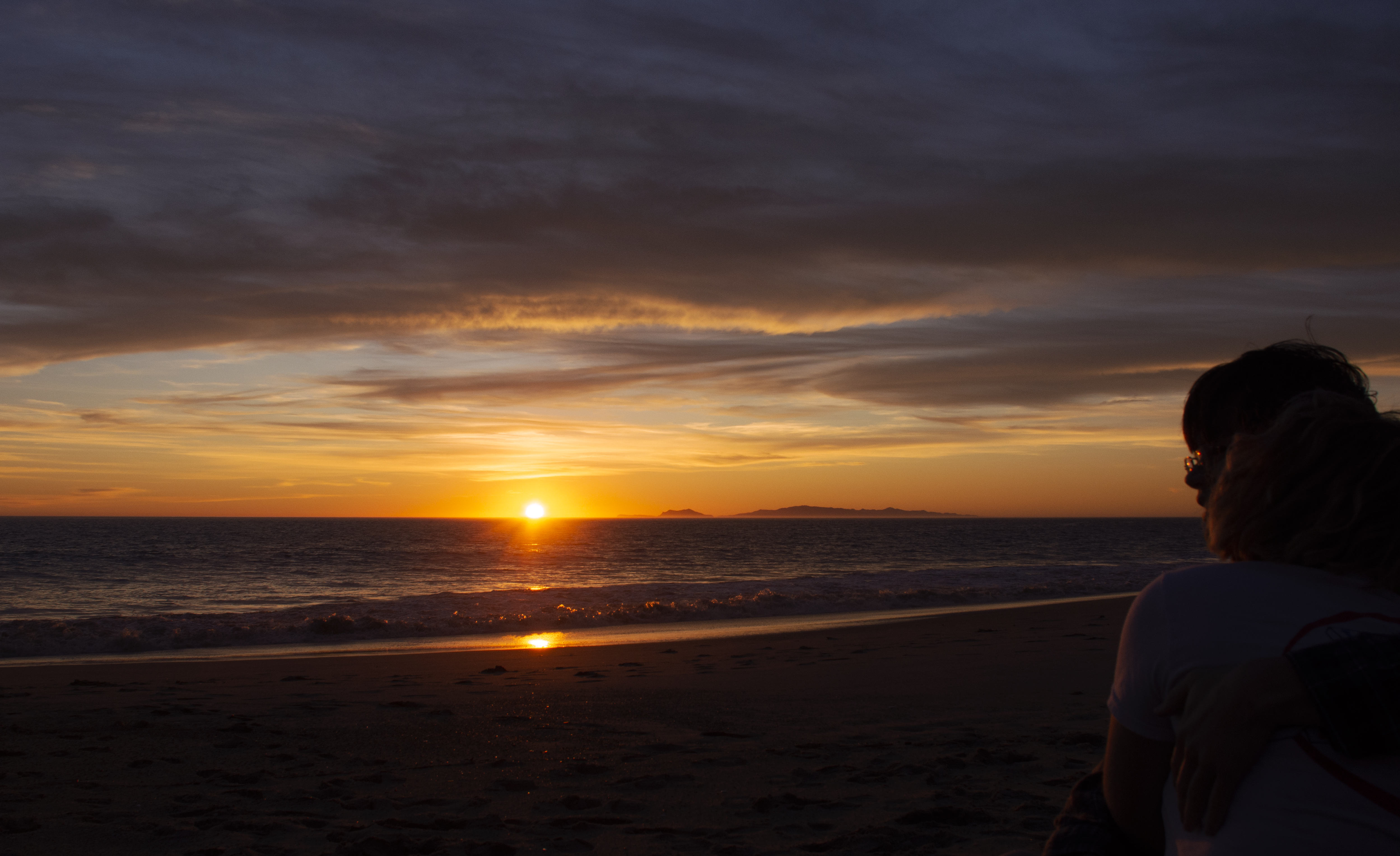 Sunset at the beach with woman on the right side facing her left side.