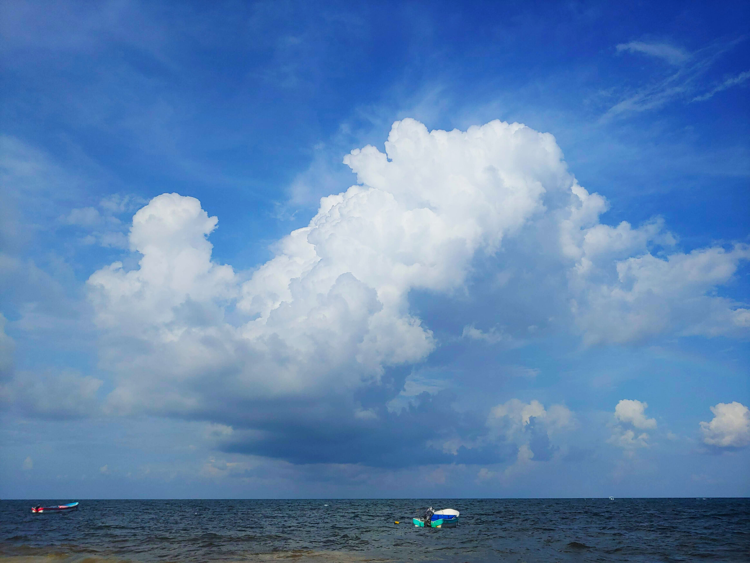 Ocean with two small boats and a large cloud in the center of the sky.