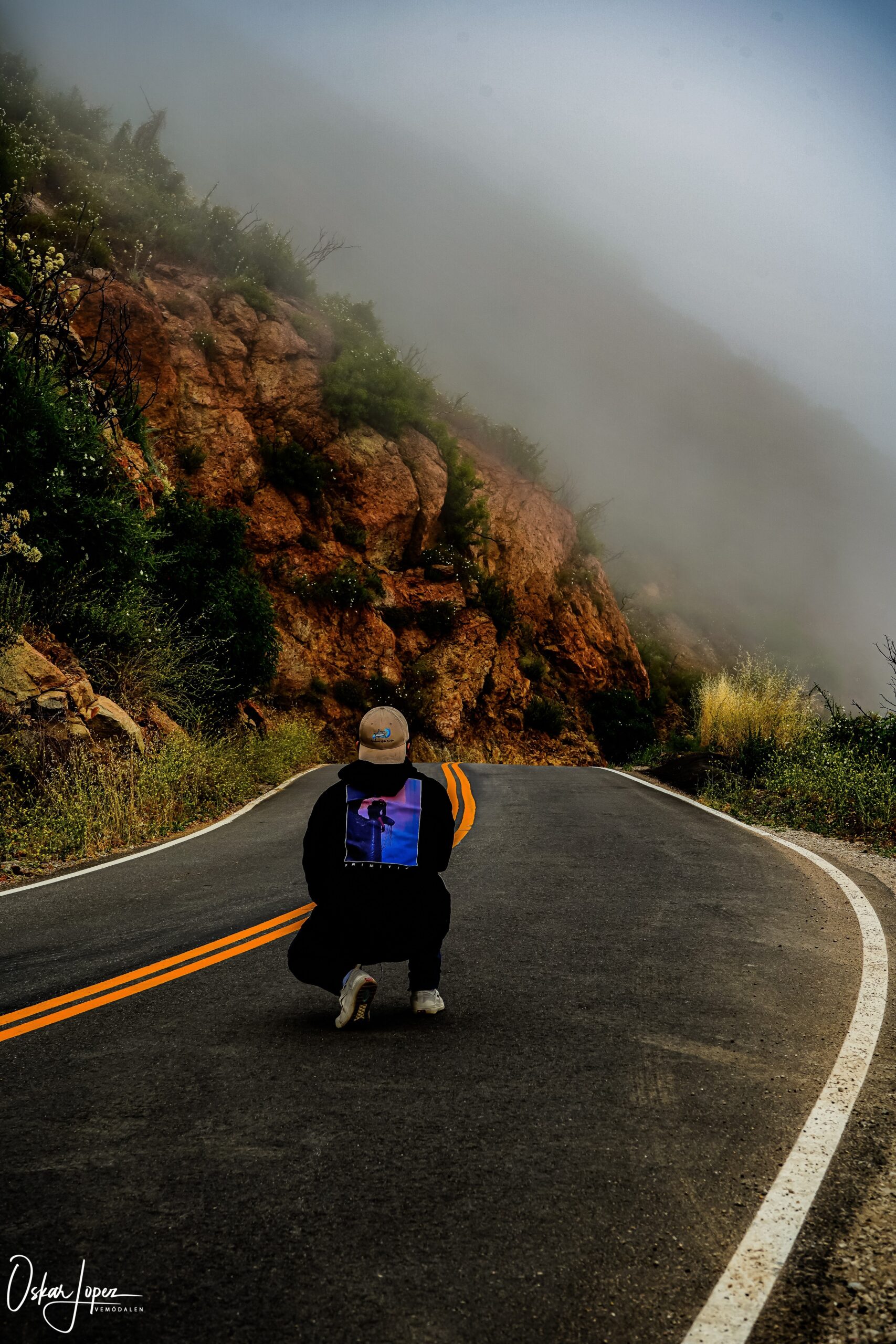 Foggy mountains behind a winding road and person kneeling down in middle of road..